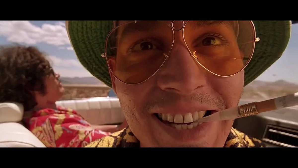 A man in aviator glasses riding in a convertible